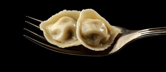 Isolated traditional Russian pelmeni ravioli and meat dumplings on a vintage fork against a black background A design and food styling concept for sale Suitable for a menu or cookbook