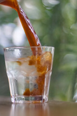 Pouring coffee into a glass of iced water on the table with blurred background	