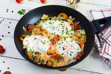 Wall Mural - Shakshuka in a frying pan.  Fried eggs with tomato, pepper, zucchini and herbs