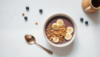 a clean flat lay capturing an elegant breakfast scene with a bowl of acai topped with granola and sliced bananas set against a smooth surface with a vintage spoon placed besid