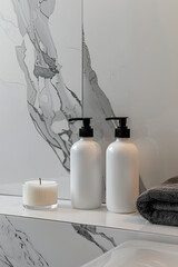 A close-up shot of two white bottles with black pump heads placed on the marble countertop in front of a modern bathroom white marble wall. A candle is also visible beside them.