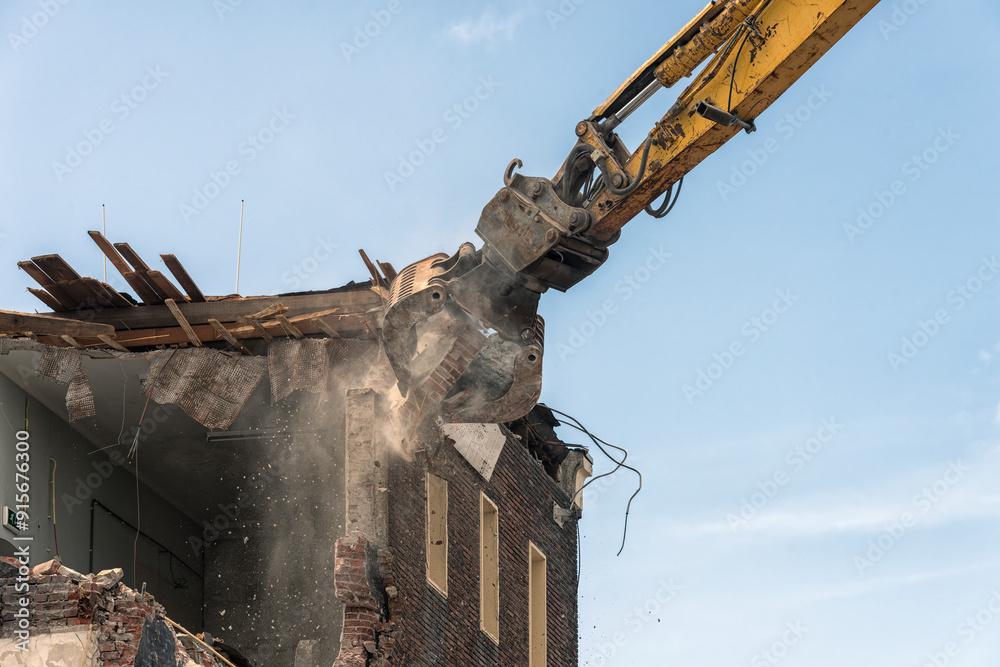 metal bucket of a demolition machine is busy demolishing a building