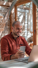 Poster - A man in a red shirt is smiling while using his cell phone and laptop