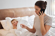 © DavisShared/peopleimages.com - Sick, thermometer and woman with phone call by child for telehealth, consultation and temperature check. Son, fever and tech with discussion on bed for medical advice, help and pediatric care at home