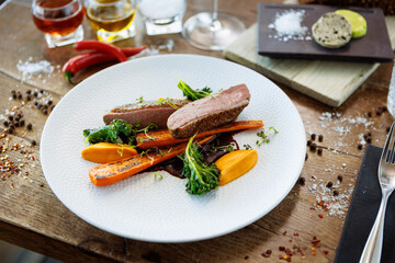 Wall Mural - Duck fillet with sweet potato cream, roasted carrots, kale, beet-port sauce on white plate. Grilled and roasted poultry closeup served on a table for lunch in modern cuisine gourmet restaurant.