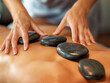 © MaxK - A woman is massaging a man's back with a series of stones. The stones are black and the woman is wearing a blue shirt