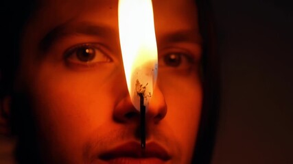 Poster - In the darkness a match is ignited and held up to a lantern causing a bright orange glow to illuminate the face of the person lighting it.