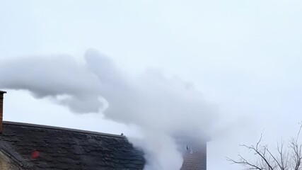 Aufkleber - A thick white cloud of smoke rises steadily from the brick chimney blending in with the overcast sky.