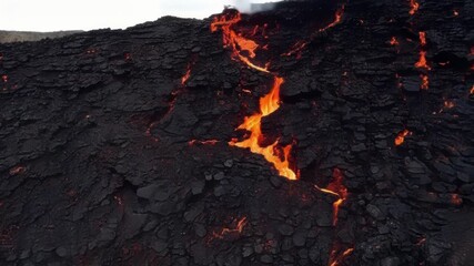 Poster - A closeup of a rocky cliff the surface cracked and blackened from repeated contact with hot lava as it flows down and shapes the landscape.