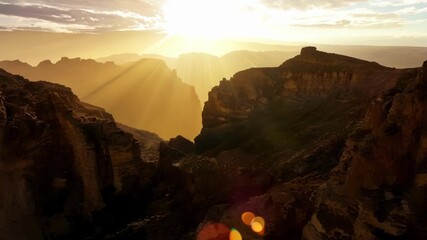 Aufkleber - The suns rays continue to stretch across the sky casting dramatic shadows on the jagged cliffs of a rocky landscape.