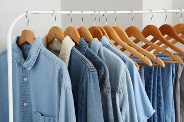 Wall Mural - Rack with different stylish denim clothes near light wall in boutique, closeup