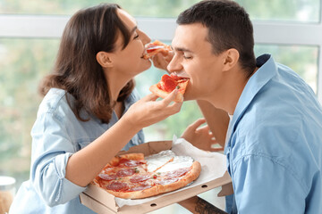 Canvas Print - Young couple eating tasty pepperoni pizza in kitchen