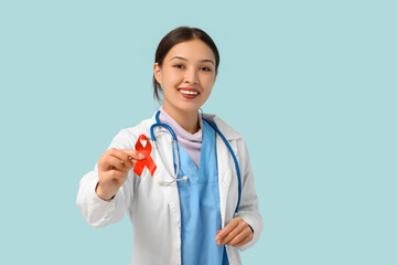 Young female doctor with red ribbon on blue background. World AIDS day concept