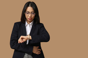 Wall Mural - Portrait of young Asian businesswoman checking time on beige background