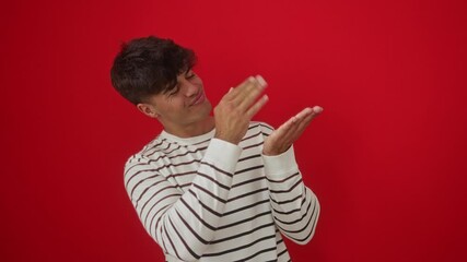 Canvas Print - Money gesture, young hispanic man wearing stripes t-shirt standing, doing hand movement, asking for salary payment, business concept over isolated red background