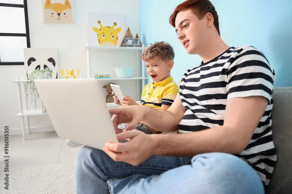 Little boy with his father using gadgets on sofa at home