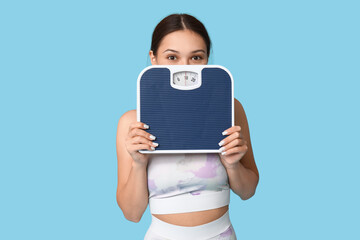 Sticker - Young woman in sportswear and with weight scales on blue background. Slimming concept