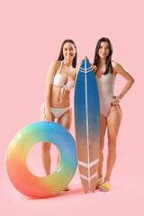 Canvas Print - Female friends in beachwear with swim ring and surfboard on pink background