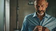 © NooPaew - Close-up of a middle-aged man buttoning a blue shirt in the bathroom, getting ready for a workday, looking excited