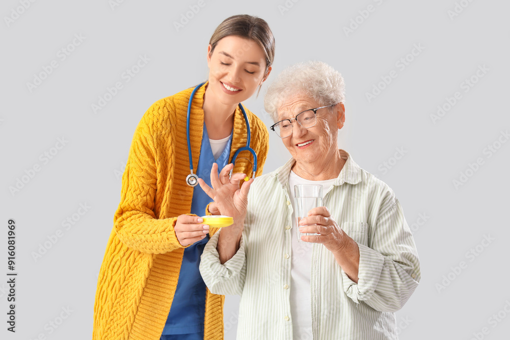 Senior woman taking pill from nurse on light background