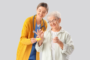 Wall Mural - Senior woman taking pill from nurse on light background