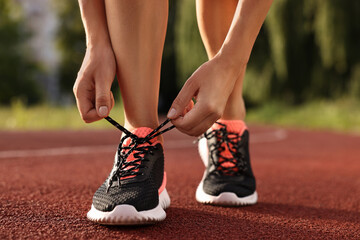 Wall Mural - Woman tying shoelace of sneaker at stadium, closeup