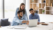 © fizkes - Three young multiethnic business colleagues watching website presentation on pc, sitting at workplace. Project manager showing online content to coworkers, pointing hand at laptop screen