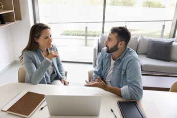 Couple of office colleagues discussing work project, job case at workplace, meeting at laptop for cooperation, brainstorming, teamwork, communication, sitting at office table, talking