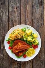 Poster - Crispy breaded fried pork chop, boiled potatoes and sauerkraut salad served on white plate on wooden table
