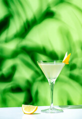 Wall Mural - Alcoholic cocktail drink with gin, vodka, aperitif, lemon zest and ice in glass on green background, hard light