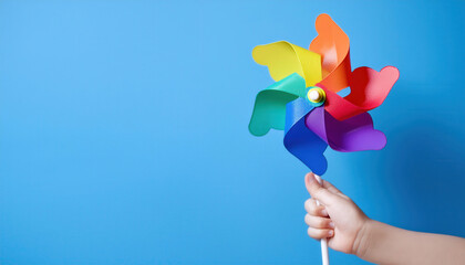 A child's hand holding a colourful windmill fan. on a blue background