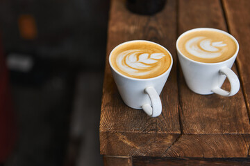 Two cups of hot coffee with milk on a wooden table outside