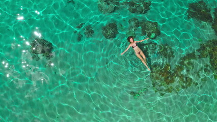 Aerial view of a young woman swimming in turquoise tropical water during summer vacation. The image evokes a sense of freedom and tranquility