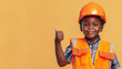 © Kanlayarawit - A cute happy smiling young African American black boy dressed like a construction worker raises his thumb up on a plain vivid orange background with copy space for text.