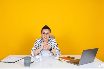 Wall Mural - Woman crumpling papers,  young brunette caucasian business woman office worker employee sit office desk over yellow studio background looking angry woman crumpling papers. Disappointed, confused.