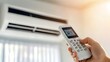 © lililia - A hand reaches for the remote control to turn on the air conditioner in a bright, clean room, creating a comfortable environment