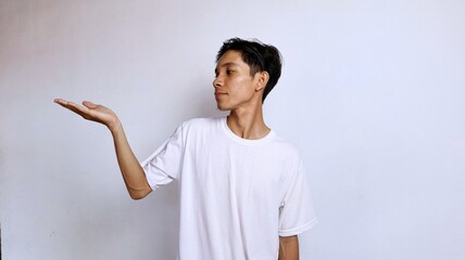 Young Asian man in white shirt smiling gesture looking at open palm isolated white background