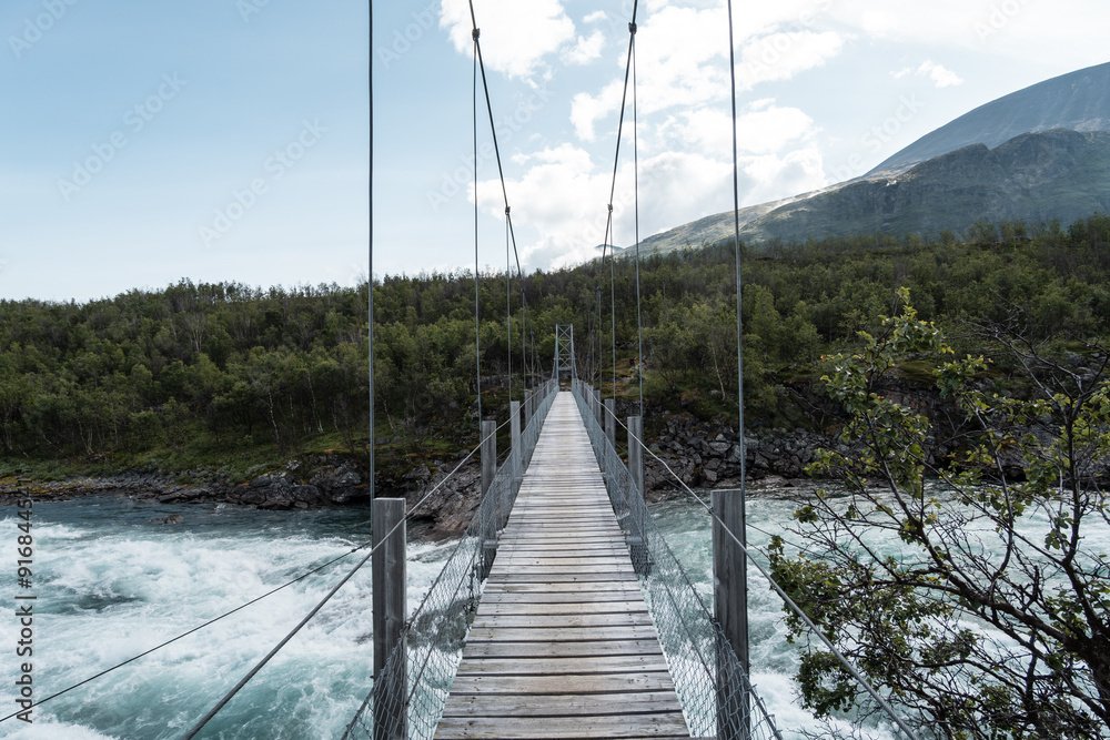 Suspension bridge over river Vuojatädno on hiking adventure trail called Padjelantaleden through National Parks of Swedish Lapland
