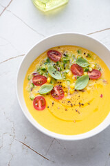 Wall Mural - Bowl of chilled gazpacho with sweet corn and yellow tomatoes, vertical shot on a white granite background, elevated view