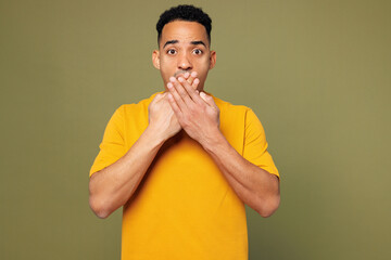 Wall Mural - Young shocked surprised man of African American ethnicity he wearing yellow t-shirt casual clothes cover mouth with hands isolated on plain pastel green background studio portrait. Lifestyle concept.