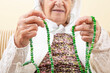© berna_namoglu - wrinkled hands of old senior muslim woman praying with green prayer beads.
