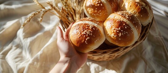 Aufkleber - A hand holds wheat ears over a basket of Kaiser or Vienna rolls set on a table with a beige linen cloth casting long shadows in the light a perfect copy space image