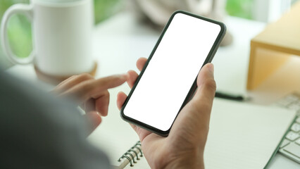 Wall Mural - Close up view of man hands holding smart phone over working desk. Blank screen for your advertise design.