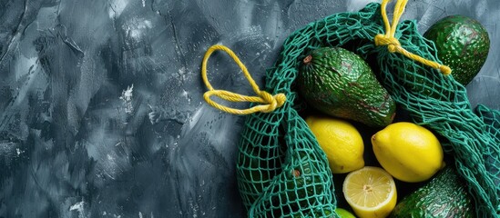 Poster - High quality photo of a green string shopping bag with fresh avocados and lemons on a grey background perfect for copy space image