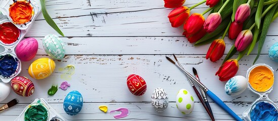 Wall Mural - Easter themed arrangement with vivid eggs paint tools and tulips on a white wood surface shot from above showcasing a copy space image