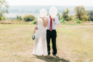 Newlyweds with white balls. Funny photo with newlyweds. The newlyweds covered their faces with white balls with a happy emoticon. Two people are holding white balloons with emoticons painted on them