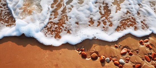 Aufkleber - Ocean waves crash against the shore leaving behind sea foam and reddish brown stones scattered along the sandy beach with a captivating view perfect for a copy space image