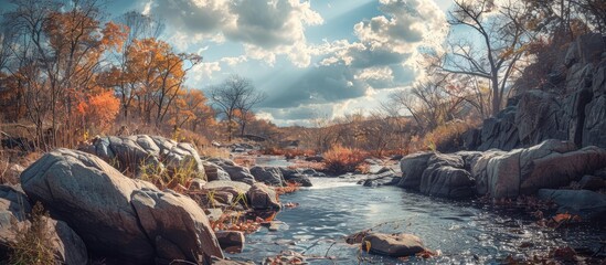 Poster - Scenic autumn view with a river cutting through rocks showcasing vibrant fall hues and leafless trees under a sky with fluffy clouds perfect for a copy space image