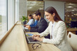 © Studio Romantic - Group of people working in company's office, friendly coworking space, or conference room interior in modern business center. Happy young woman in suit sitting at table, working on laptop and smiling
