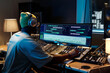 © pressmaster - African American music producer working with mixing equipment in well-lit studio filled with various audio devices, wearing headphones and focused on monitors
